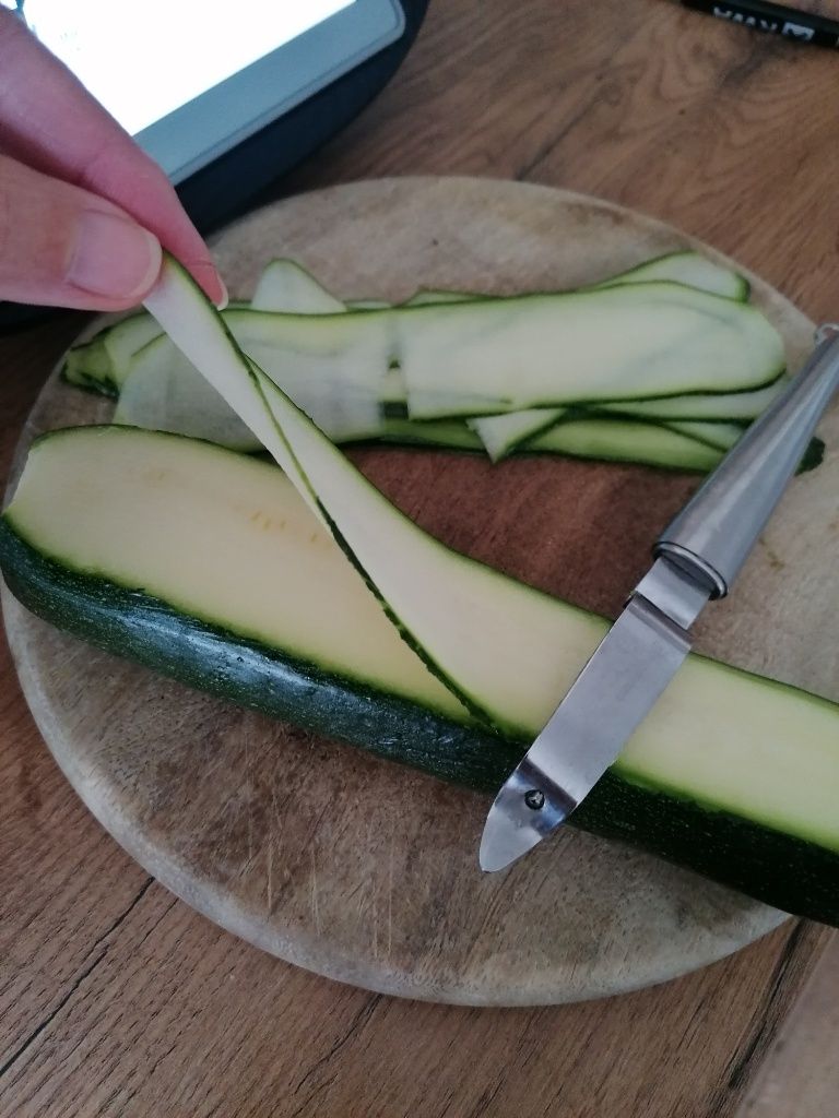 Mit einem Sparschäler werden dünne lange Scheiben von einer Zucchini abgeschnitten