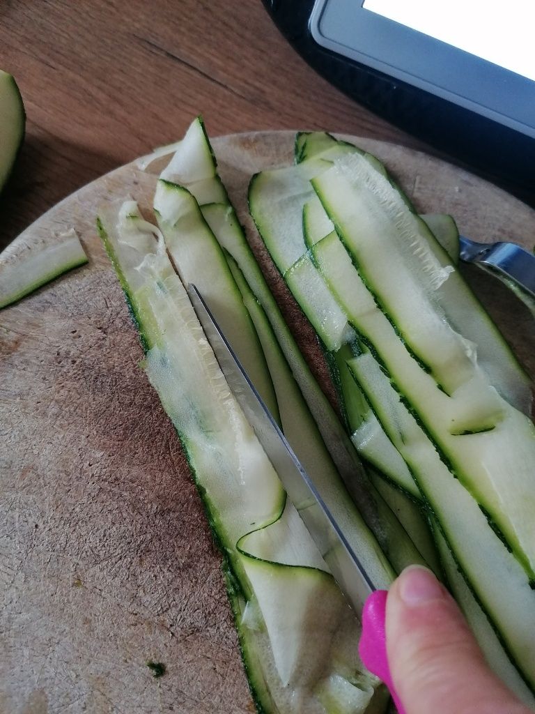 Schmale Zucchinischeiben werden auf einem Schneidbrett zu etwas 1 cm breiten Streifen geschnitten