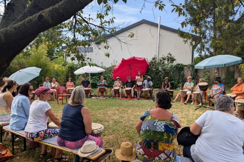 33 Menschen sitzen im Garten im Kreis. Jeder hat vor sich eine Djembe.