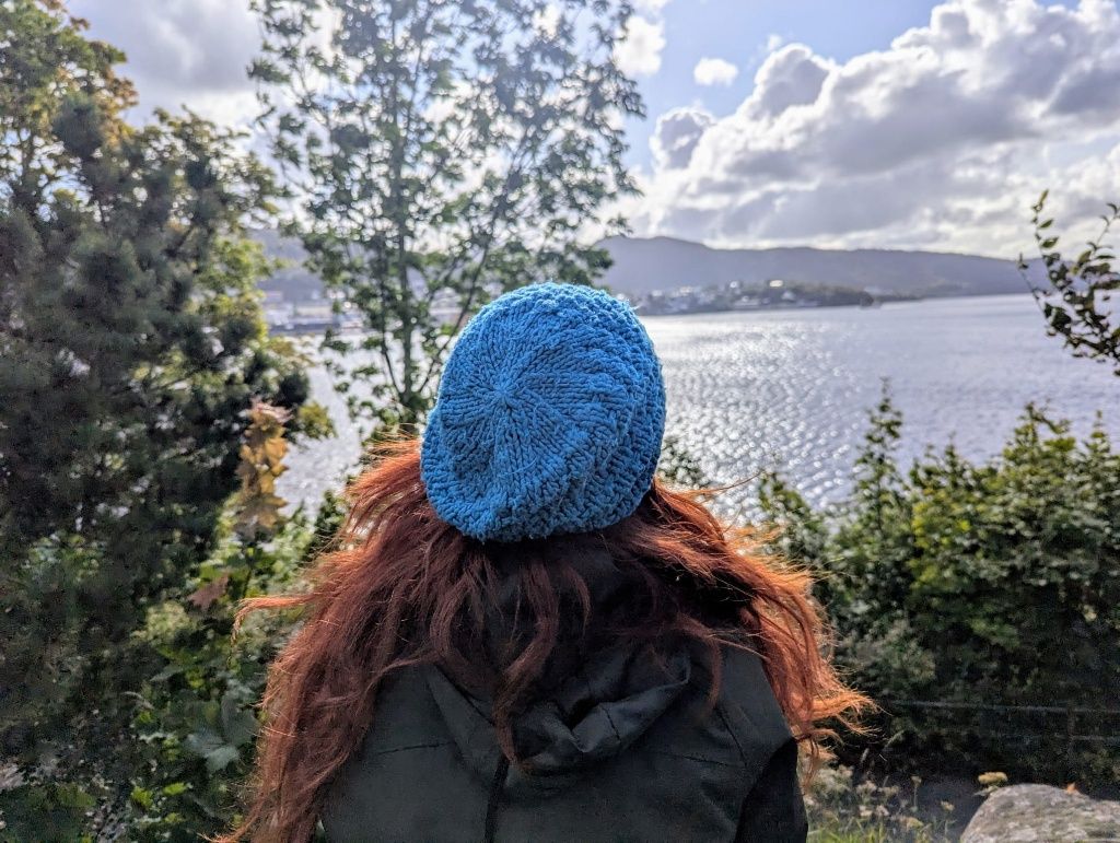 Karin von hinten mit blauer Haube, blickt aufs Meer