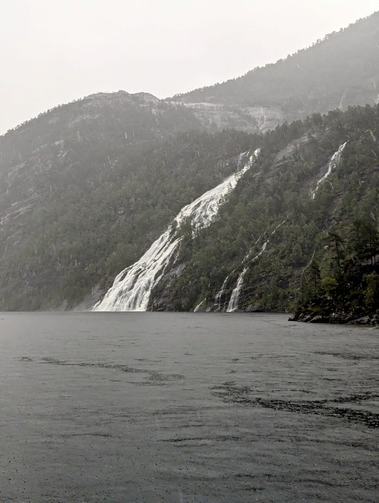 Bewaldeter, steil abfallender Berg mit Wasserfall, der im Meer endet