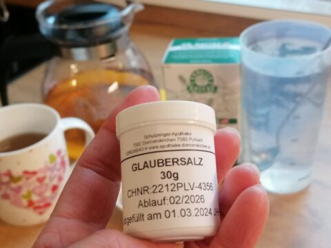 Kleine Dose mit 30 g Glaubersalz, im Hintergrund ein Häferl mit Pfefferminztee